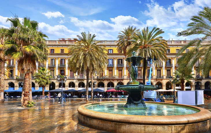 Royal area in Barcelona, Spain. Fountain with statues and high palm trees among traditional Spanish architecture at main central square of old town. Summer landscape with blue sky and clouds.